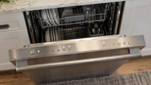 The lit control panel along the top edge of an open stainless steel dishwasher door seen from above