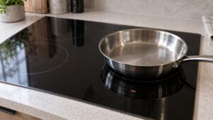 A black glass induction cooktop with a stainless steel pan resting on one zone while that zone display shows a dash instead of a power level