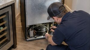 A technician inspecting the back of an undercounter wine cooler near its compressor