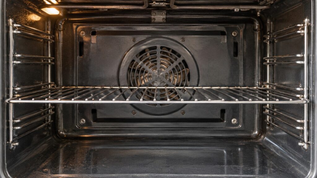 The back wall of a built-in oven cavity showing the circular fan cover behind the rack