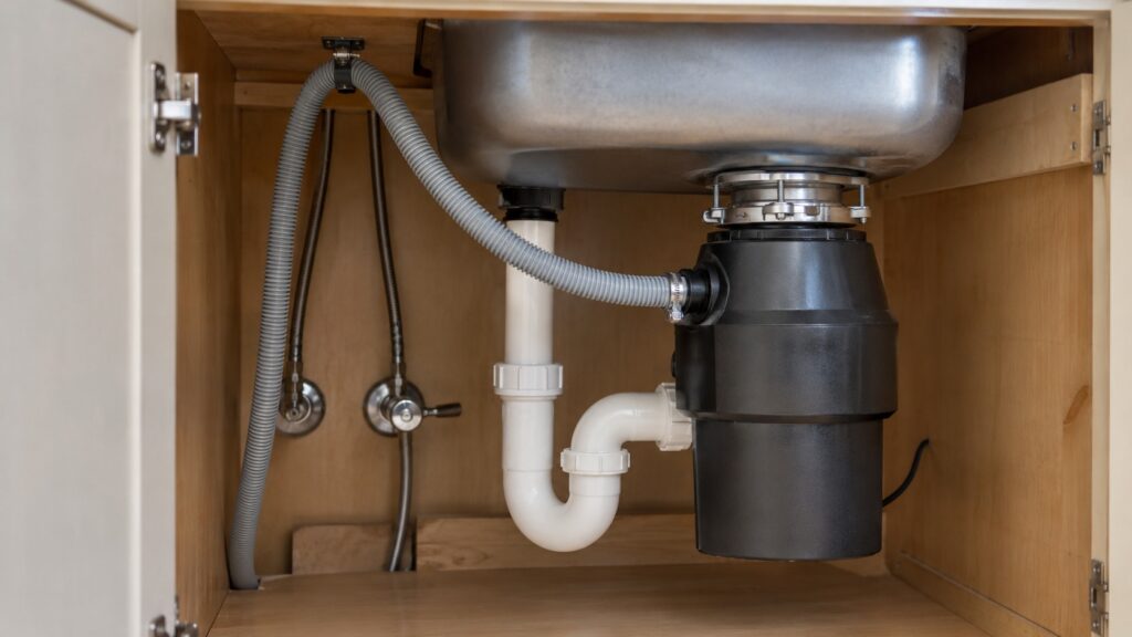The cabinet under a kitchen sink with a dishwasher drain hose routed up to a clamp and over to the disposal inlet